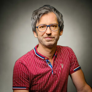 Die Fotografie ist ein Portrait des freischaffenden Künstlers und Fotografen Marcel Noack. Er ist Vorstandsmitglied der VG Bild-Kunst und repräsentiert die Berufsgruppe 1 (bildende Kunst). Die linke Schulter leicht nach hinten gerückt, sieht er freundlich lächelnd in die Kamera. Er hat braune Augen, graumelierte Haare mit einer kleinen Tolle vorne rechts und einen Dreitagebart. Er trägt eine modische blaue Brille und ein rotes Poloshirt mit kurzen Ärmeln und einem kleinen Stehkragen. Die ersten zwei Knöpfe sind geöffnet. Das Shirt hat ein Muster aus regelmäßig angelegten weißen Kreuzchen sowie blau-weiß-roten Streifen an Kragen und Ärmelbündchen, abwechselnd hellblau-dunkelblau gestreifter Knopfleiste. An der Brust ist ein aufgesticktes Markenzeichen zu erkennen. 
